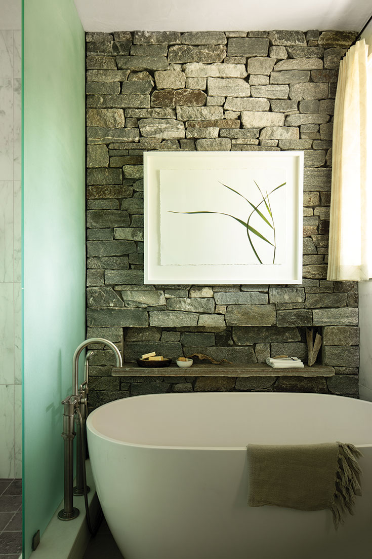 The same stone used to face the fireplace also accents the primary bathroom, adding a rustic note amid the spa-like setting.